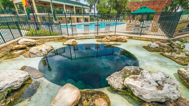 A hot spring area with a central pool surrounded by rocks, a fenced pool area in the background, and a pavilion. - Charming Retreat w/ Bikes (Green Cove Springs)