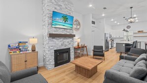 A modern living room with a fireplace, grey sofas, a wooden coffee table, and a dining area with a table and chairs. - Charming Retreat w/ Bikes (Green Cove Springs)