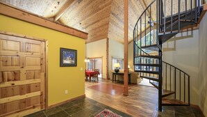 A spacious interior with a wooden ceiling, a spiral staircase, a dining area, and a large wooden door.
