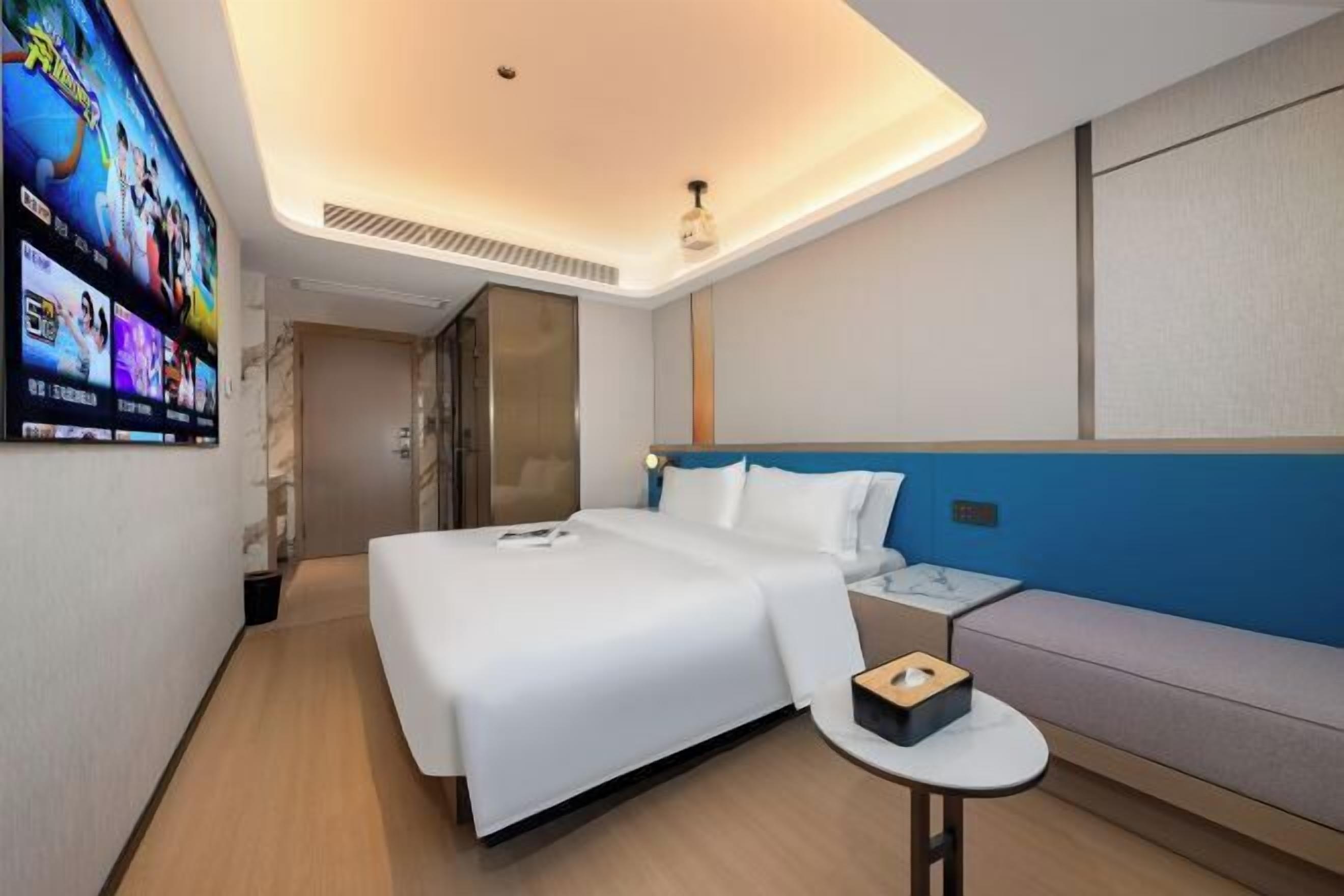 A modern hotel room with a large bed, a bedside table, a sofa, and a TV mounted on the wall.
