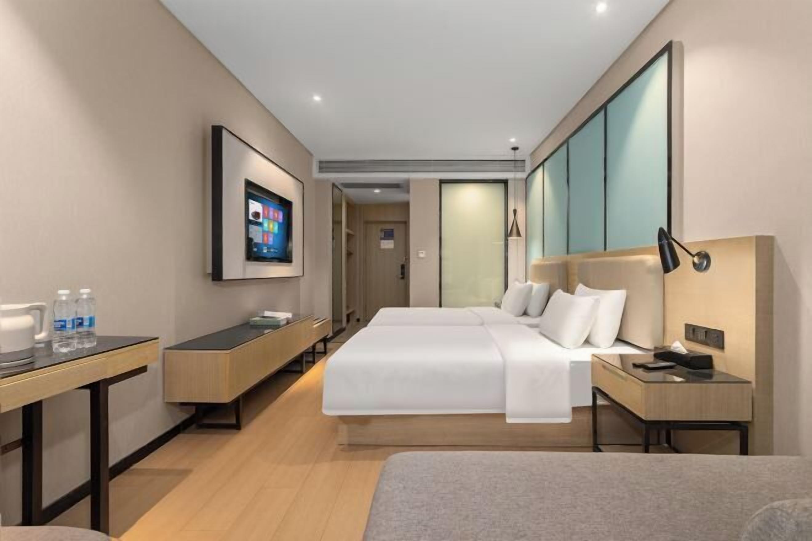 A modern hotel room with two beds, a desk, a TV, and a minibar.