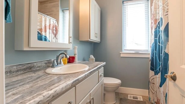 A bathroom with a marble sink, a toilet, a mirror, and a window with blinds. - Pet-Friendly Home Near IU Campus (Bloomington)