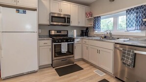 Una cocina moderna con armarios blancos, electrodomésticos de acero inoxidable, un ventanal con cortinas estampadas y un tapete negro en el suelo.