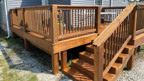 Una terraza de madera con una escalera que lleva a una casa de revestimiento gris.