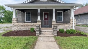 Una casa de dos pisos con porche delantero, cimientos de piedra y una puerta roja.