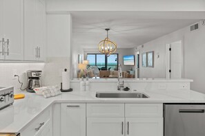 Una cocina moderna con armarios blancos, un lavamanos de acero inoxidable y una cafetera.