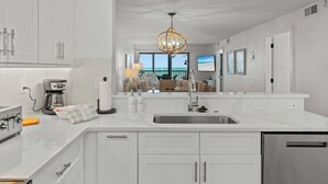 Una cocina moderna con armarios blancos, un lavamanos de acero inoxidable y una cafetera.