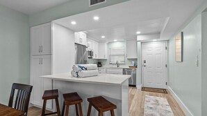 Una cucina moderna con mobili bianchi, un'isola centrale con sgabelli e un'area pranzo con tavolo e sedie in legno.