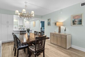 A dining area with a wooden table and chairs, a chandelier, and a cabinet with decorative items. - Sand Pointe 123 | Peaceful Gulf-View Escape | 2BR Condo Perfect for Families (Sanibel)