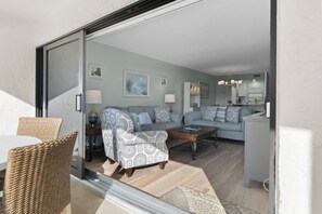 A living room with a sofa, armchairs, a coffee table, and a dining area with wicker chairs and a table. - Sand Pointe 123 | Peaceful Gulf-View Escape | 2BR Condo Perfect for Families (Sanibel)
