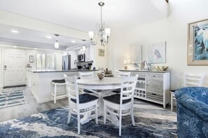A modern kitchen with white cabinetry, a central island, and a dining area with white chairs.