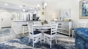 Une cuisine moderne avec des meubles blancs, un îlot central et un coin repas avec des chaises blanches.