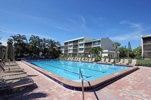 A swimming pool with lounge chairs and a building in the background. - Reimagined 2BR/2BA Gulf-View Condo with Luxe Amenities (Sanibel)