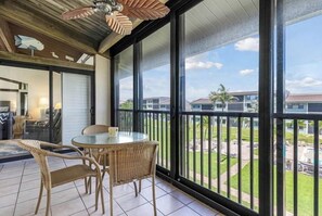 A balcony with wicker furniture and a glass table, overlooking a residential area.