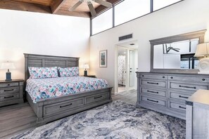 A bedroom with a large bed, a dresser, a mirror, and a door leading to another room.