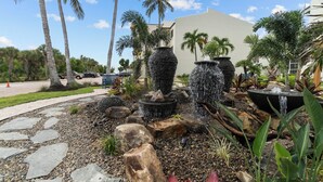 A landscaped garden with a stone pathway, palm trees, and a water feature with multiple stone planters.