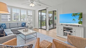 A modern living room with a grey sofa, wicker chairs, a coffee table, and a TV displaying a beach scene.