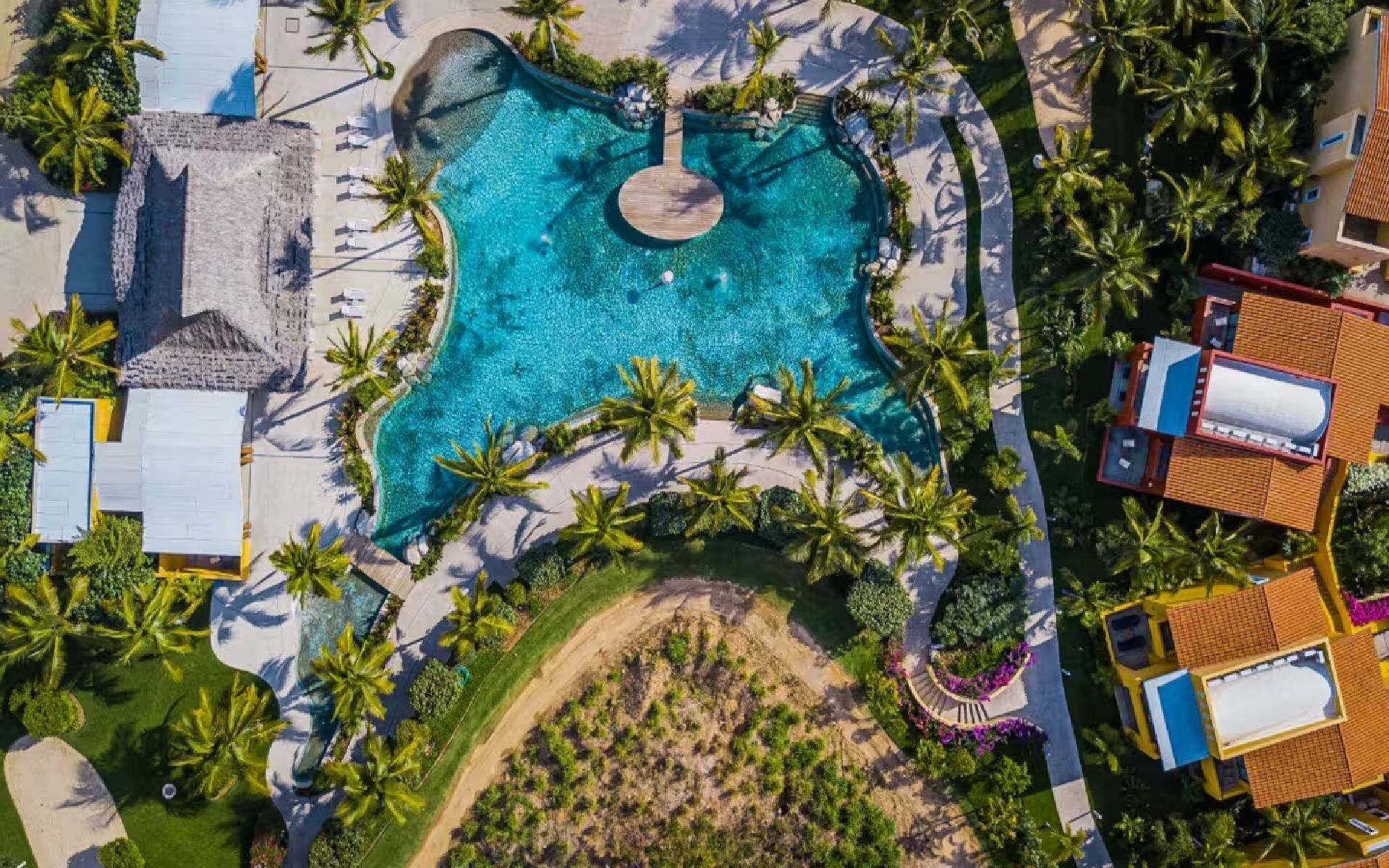 Vista aérea de un complejo turístico con una piscina central rodeada de palmeras y tumbonas.