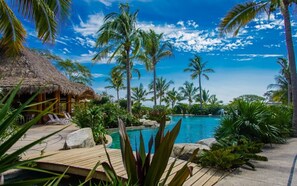 A tropical resort with a pool, palm trees, and a thatched-roof hut. - Casa Puerto Bahía Ocean View Pool and gym (La Cruz de Huanacaxtle)