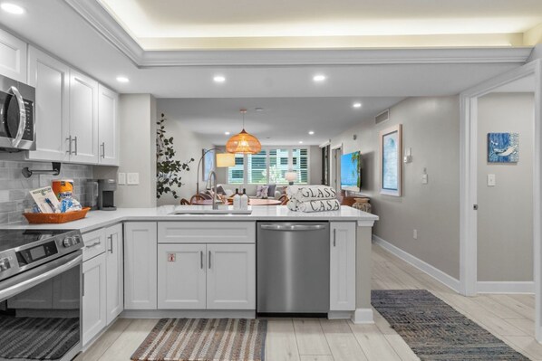 A modern kitchen with white cabinetry, a central island, a dishwasher, and a microwave.