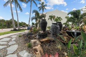 A landscaped garden with a stone pathway, palm trees, and a water feature with multiple stone planters.