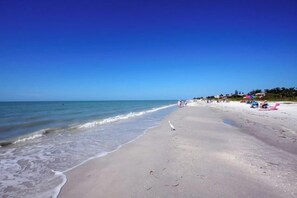 A beach with a clear sky, calm sea, and people relaxing on the sand.
