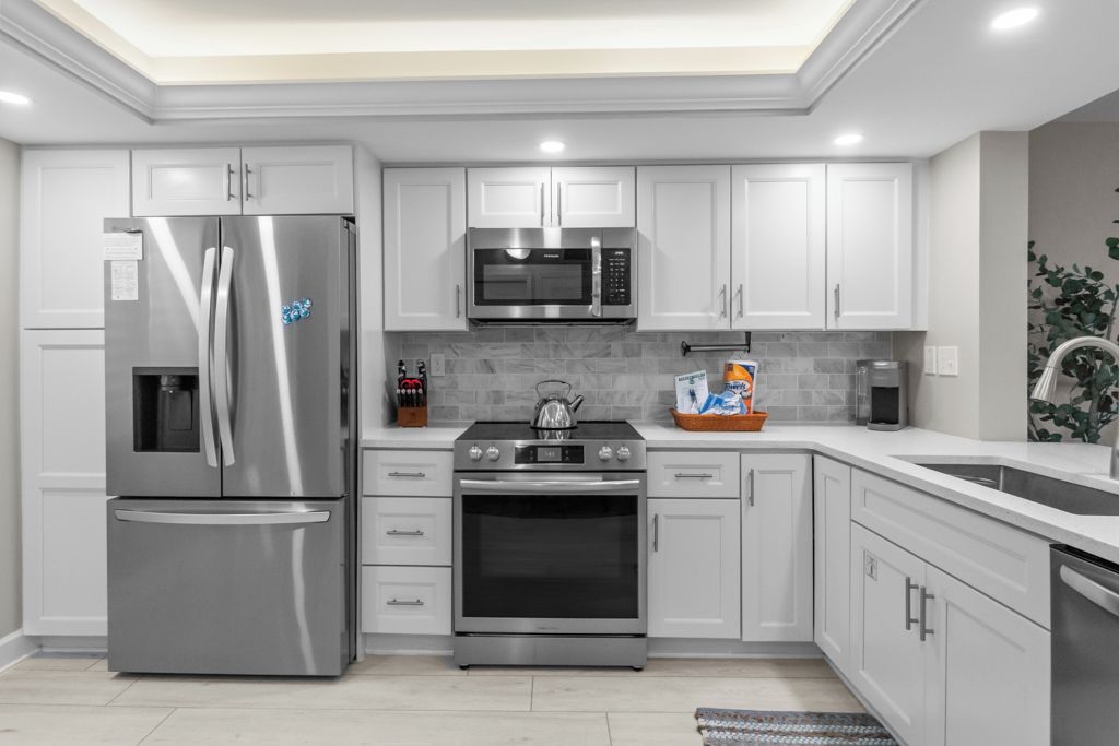 Una cocina moderna con electrodomésticos de acero inoxidable, armarios blancos y salpicadero de azulejos.