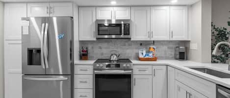 A modern kitchen with stainless steel appliances, white cabinetry, and a tiled backsplash.