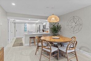 A dining area with a round wooden table, six chairs, a hanging light fixture, and a wall-mounted compass decoration.