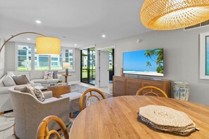 A modern living room with a sofa, coffee table, dining table, and TV.