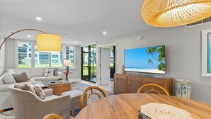 A modern living room with a sofa, coffee table, dining table, and TV.