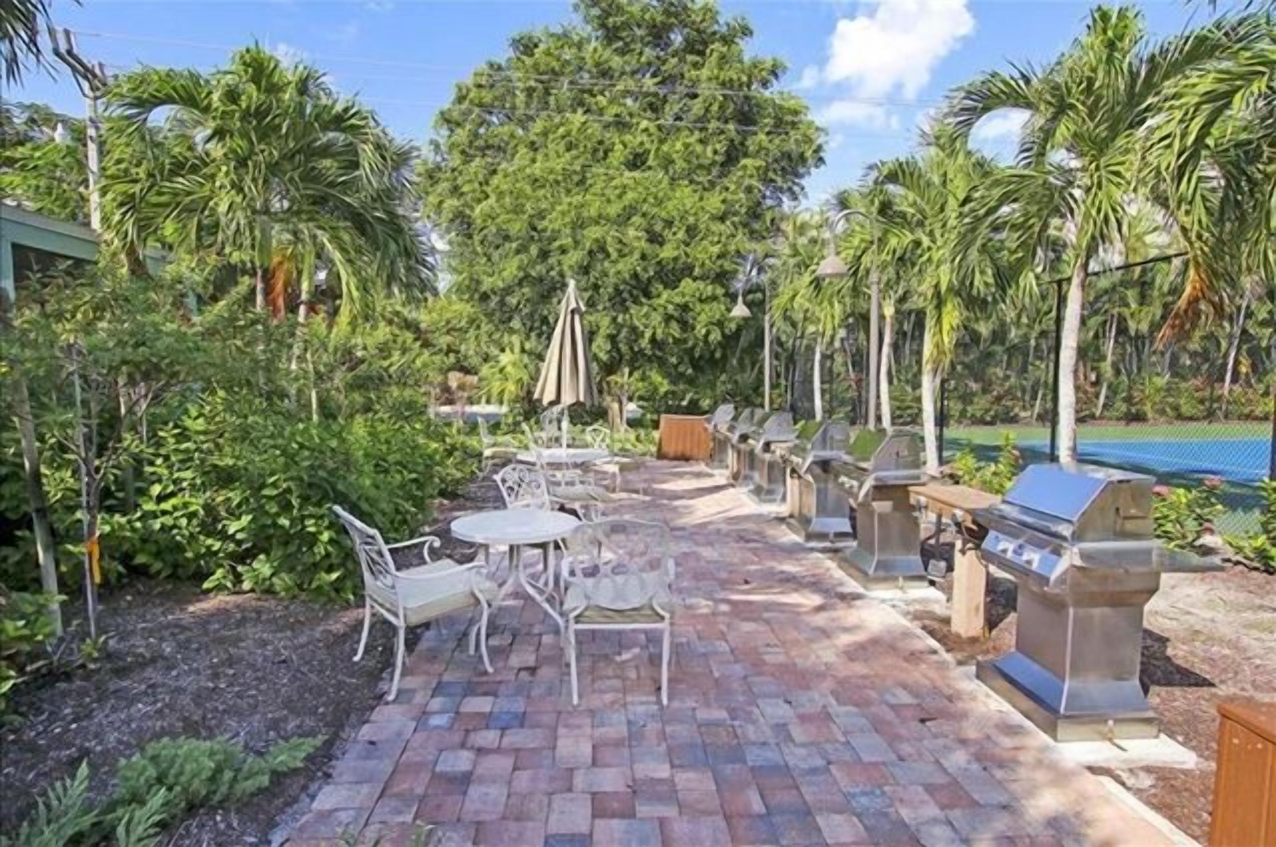 Une terrasse extérieure avec un sol en briques, des chaises en métal blanc et un espace barbecue.