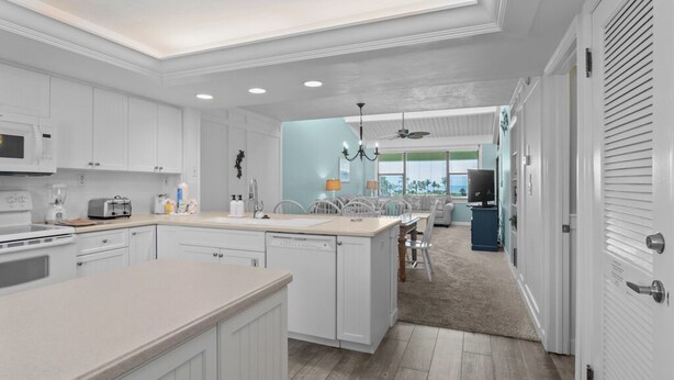 A modern kitchen with white cabinetry, a central island, and a dining area with a blue accent wall.