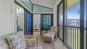A spacious balcony with a wooden floor, wicker furniture, and a glass door leading to an interior room.