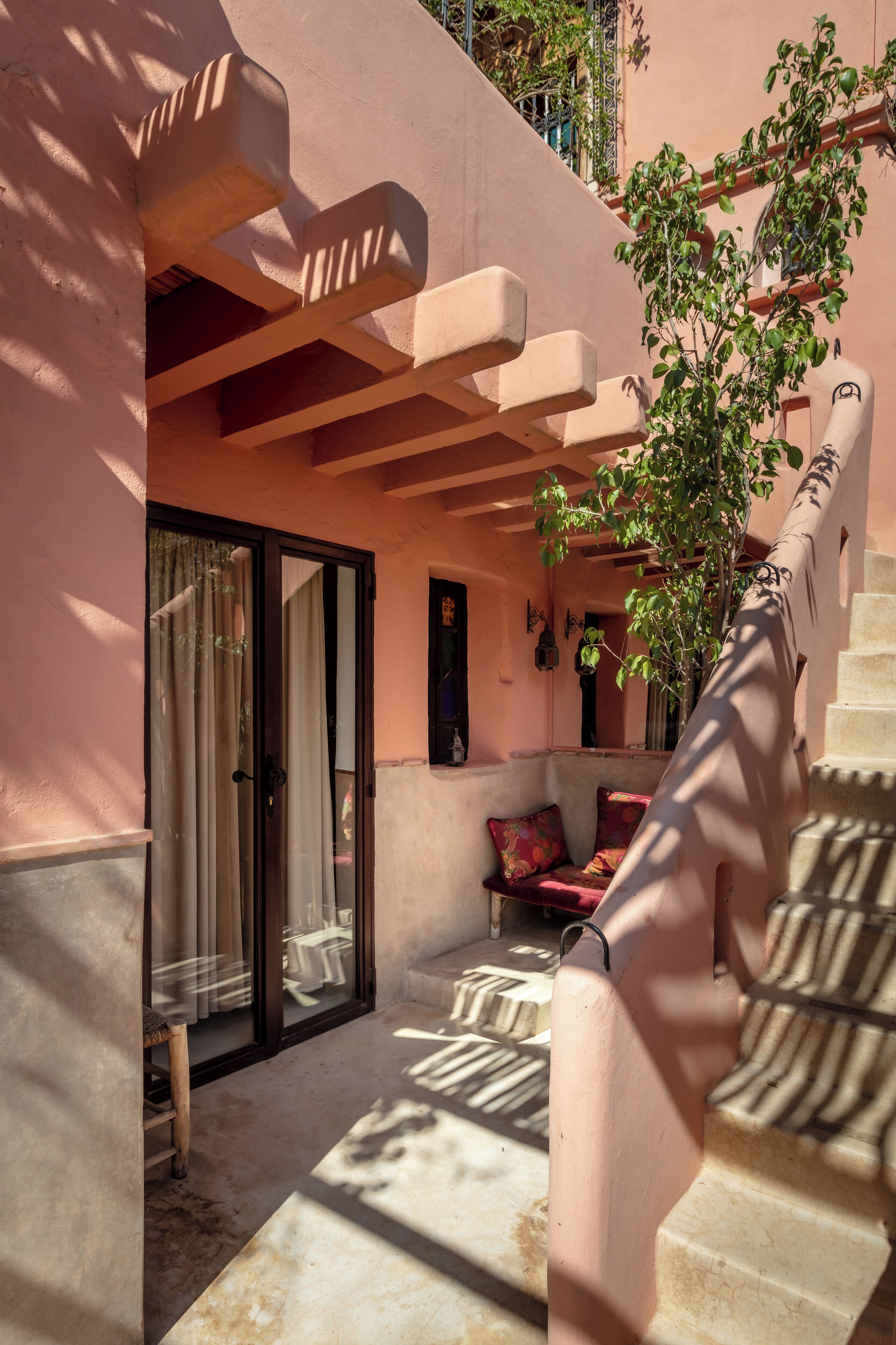 A sunlit courtyard with a staircase, a cushioned seating area, and a potted plant.