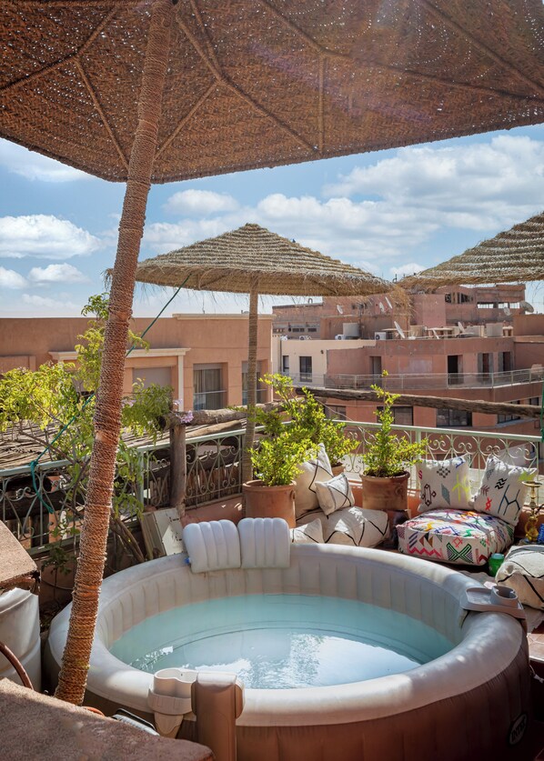 A rooftop terrace with a hot tub, potted plants, and outdoor furniture under a thatched umbrella. - The Penthouse Marrakech (Marrakech)