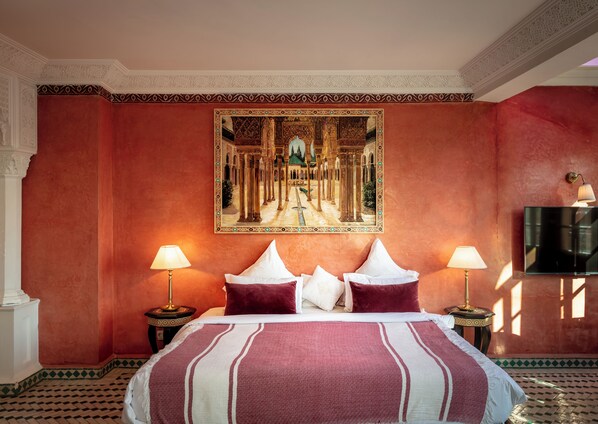 Een hotelkamer met een groot bed, twee bedlampen, een televisie en een wandeling schilderij van een architecturaal tafereel.
