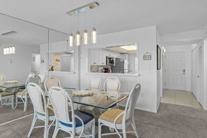 Un comedor moderno con una mesa de vidrio, sillas de mimbre blanco e iluminación colgante.
