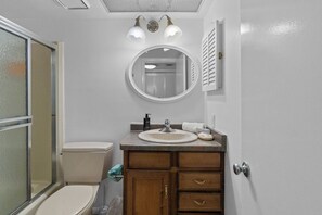 Un baño con inodoro, lavamanos, tocador con cajones, un espejo y zona de ducha.
