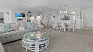 Ein modernes Wohnzimmer mit einem grauen Sofa, einem Glastisch und einem Essbereich mit weißen Stühlen und einem Tisch.