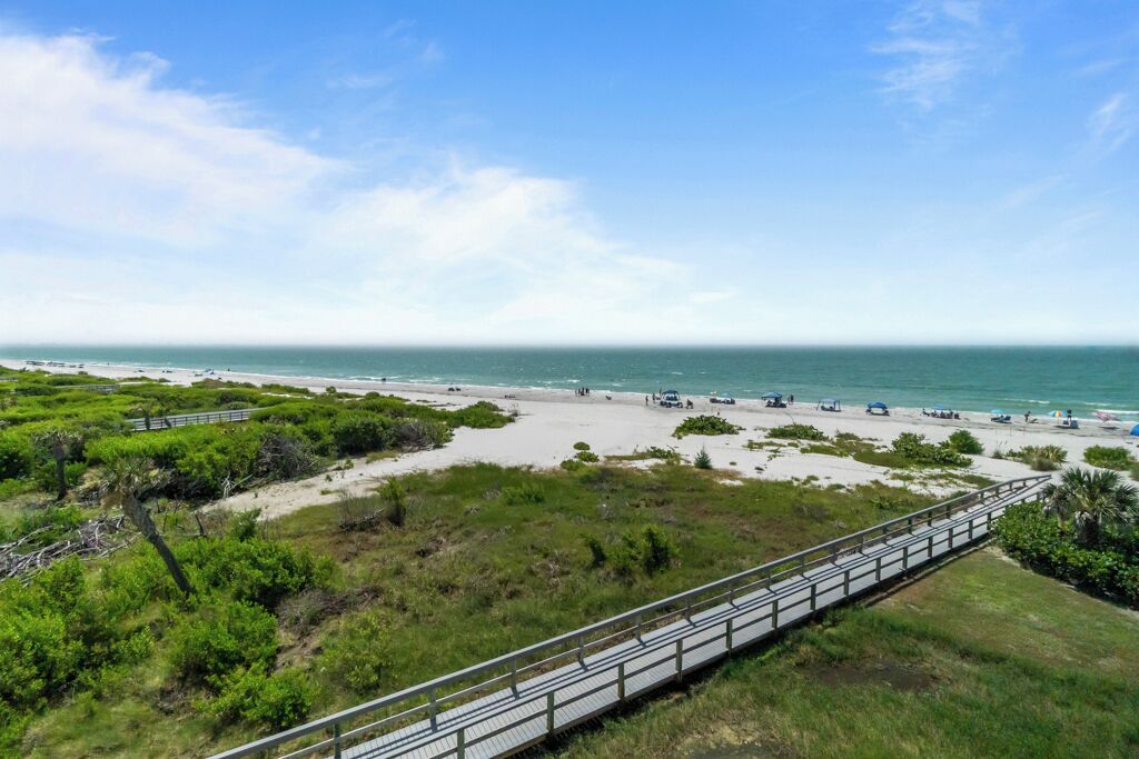 Vista costera con playa, una pasarela de madera y cielo despejado.