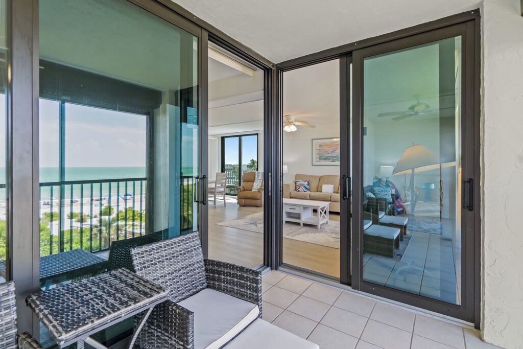 A balcony with a view of the ocean, a seating area with a table, and a sliding glass door leading to an interior living space.