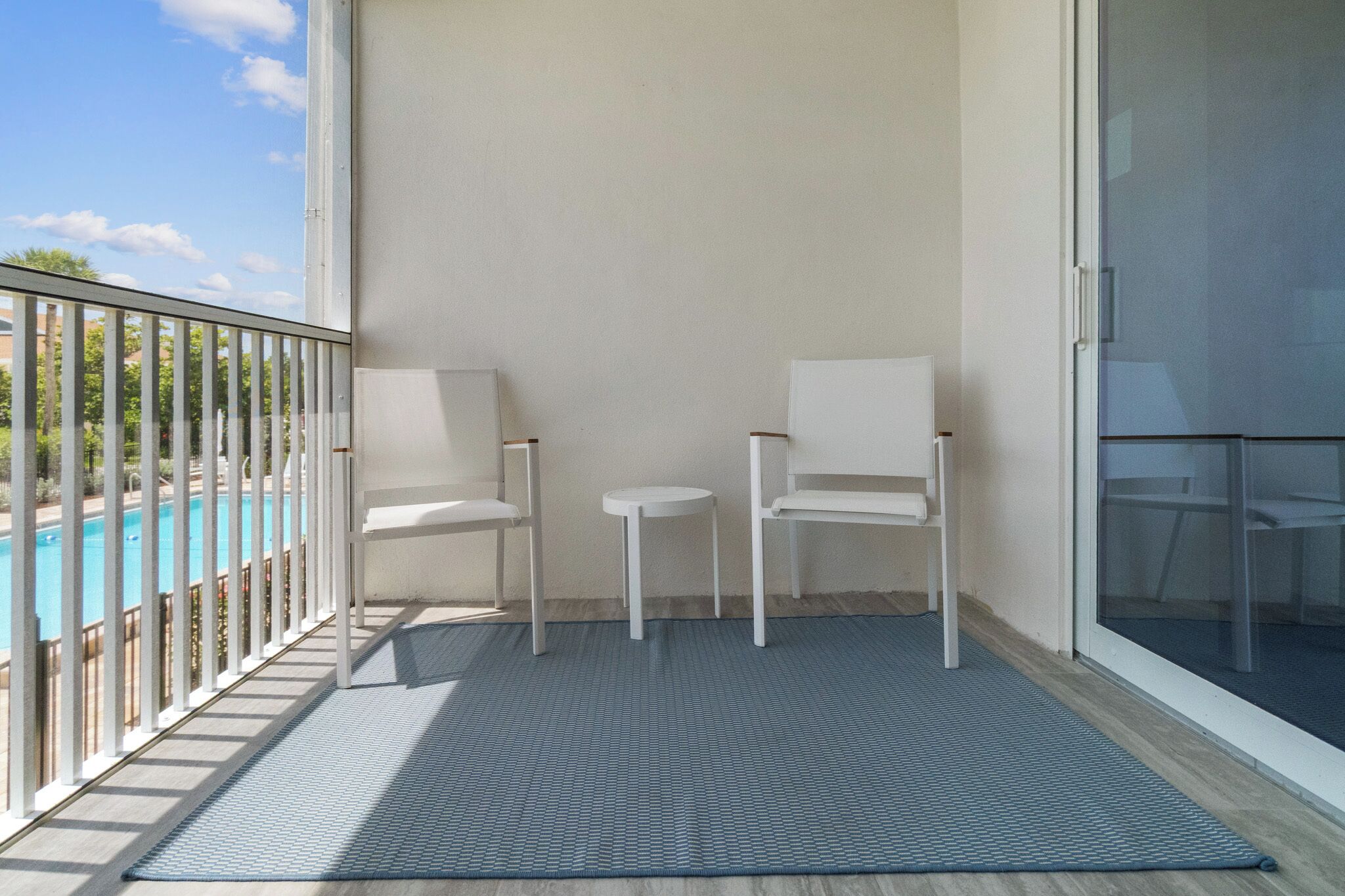 A balcony with two white chairs, a small table, and a view of a swimming pool.
