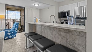 A modern kitchen with a white countertop, stainless steel appliances, and a large window overlooking a balcony.