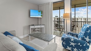 A modern hotel room with a balcony, a flat-screen TV, a small desk, and a sofa with a star pattern.