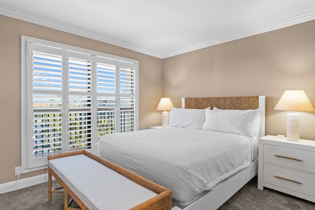 Un dormitorio con cama, dos mesitas de noche con lámparas, una ventana con persianas y vistas al exterior.