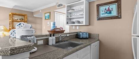 A kitchen with granite countertops, white cabinets, a built-in sink, and a water dispenser.