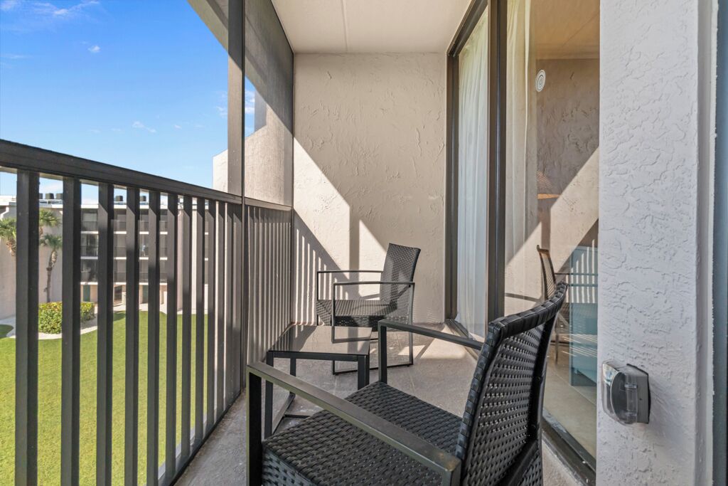 Een balkon met een glazen deur, een kleine tafel en twee rieten stoelen.