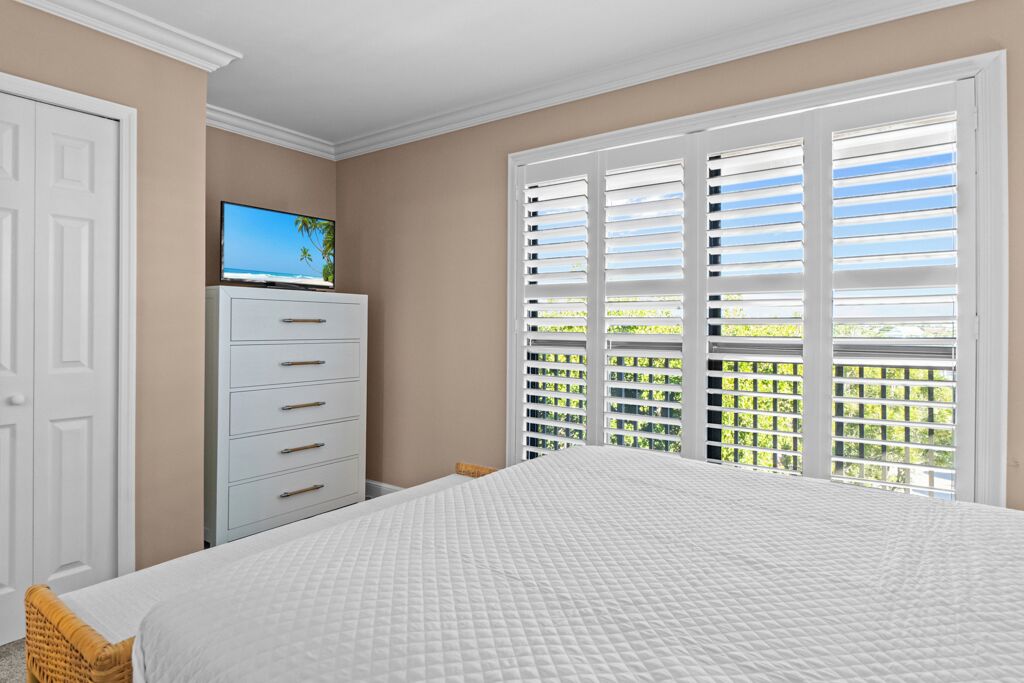 Quarto com cama, penteadeira, televisão e janela com persianas.