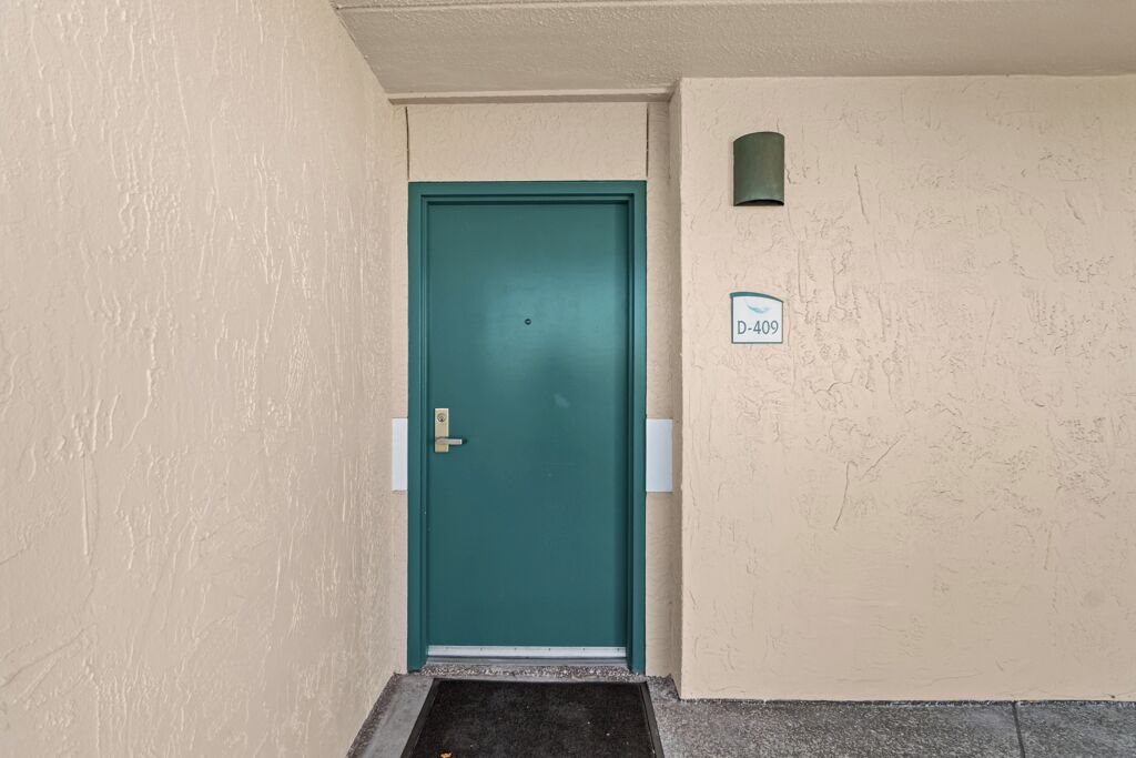 A teal door with a small mailbox and a sign reading "D-409" on the wall beside it.